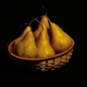 5 golden portrait pears with russet skin arranged in a basket against a black background